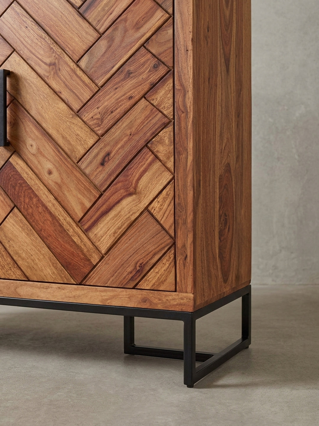Detailaufnahme eines schwarzen Metallgriffs am Schuhschrank, montiert auf dem detailreichen Fischgrätmuster der Tür aus massivem Sheesham-Holz._