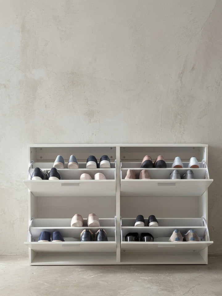 Nahaufnahme der edlen Aluminiumgriffe am weißen Schuhschrank. Die minimalistischen, geradlinigen Beschläge heben sich dezent von der mattweißen Holz-Oberfläche der Flurkommode ab._