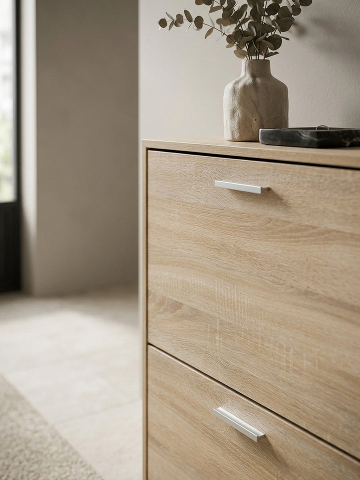Detailaufnahme der authentischen Sonoma Eiche Holzmaserung des Schuhschranks. Die matte Oberfläche der Flurkommode kontrastiert elegant mit den modernen Aluminiumgriffen._