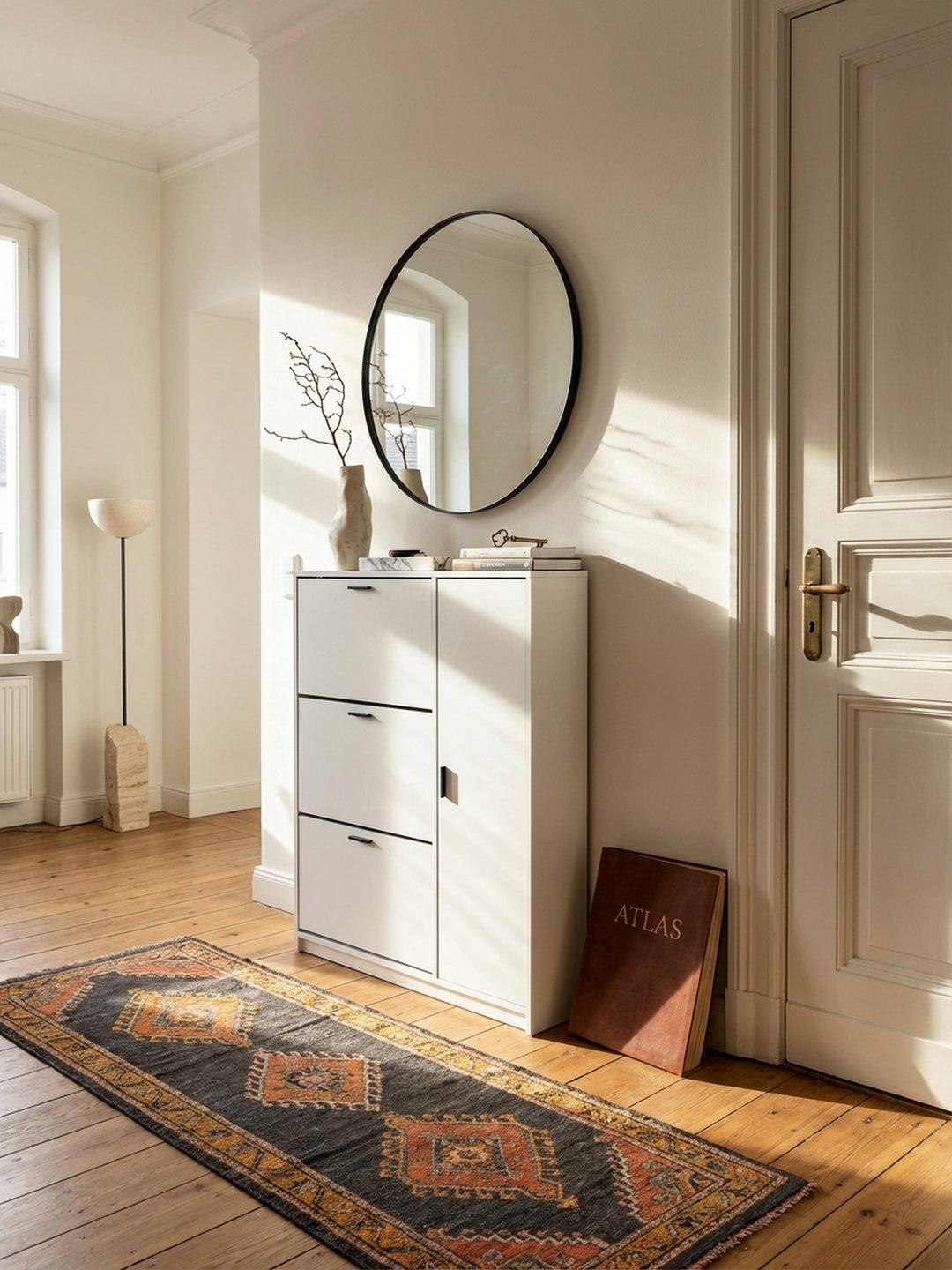 Moderner Schuhschrank in Weiß mit schwarzen Griffen in einem hellen Altbau-Flur auf breiten Eichendielen, dekoriert mit einer Keramikvase und Marmorschale._