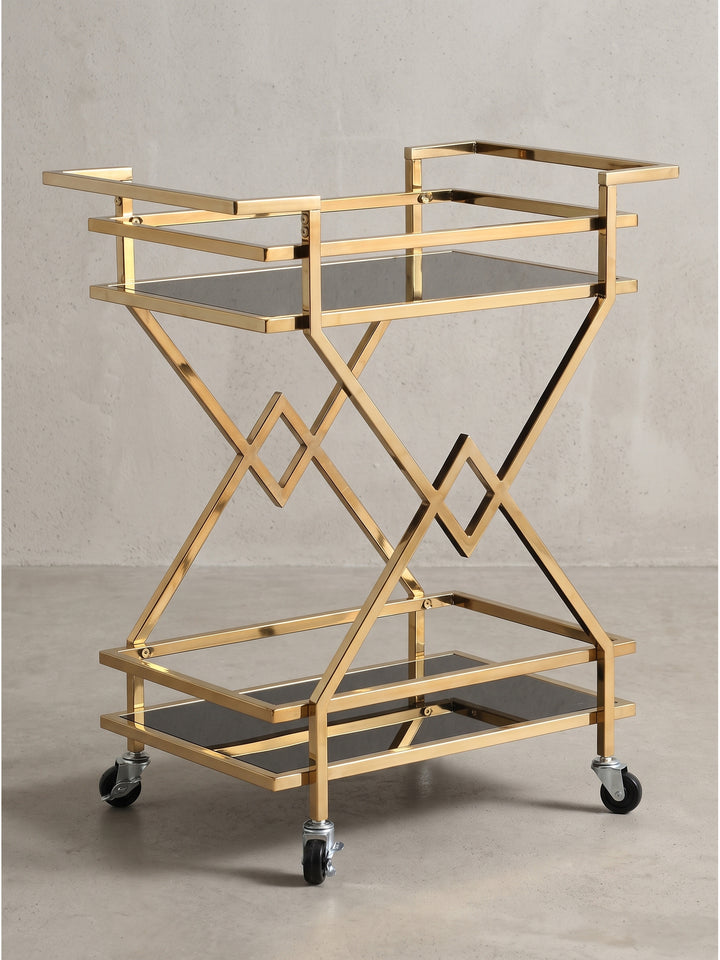 Geometrischer Servierwagen aus Metall in Gold und schwarzem Sicherheitsglas in der Frontansicht mit seitlichen Griffen._