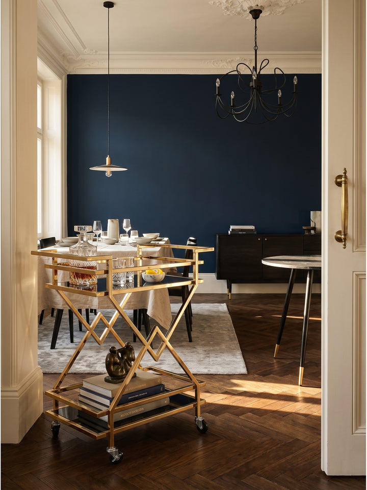 Eleganter Servierwagen aus goldfarbenem Stahl und schwarzem Glas 65x80x40 cm in luxuriösem Art-Deco-Wohnzimmer vor nachtblauer Wand._
