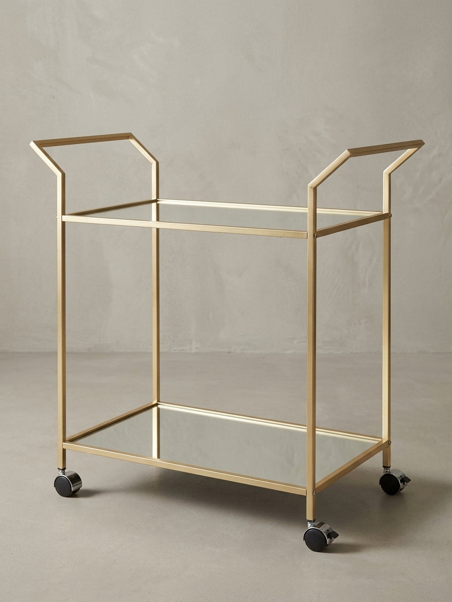 Der Küchenwagen in Gold aus der 3/4-Perspektive, die die Tiefe der zwei verspiegelten Ablageflächen und die stabilen Rollen zeigt._