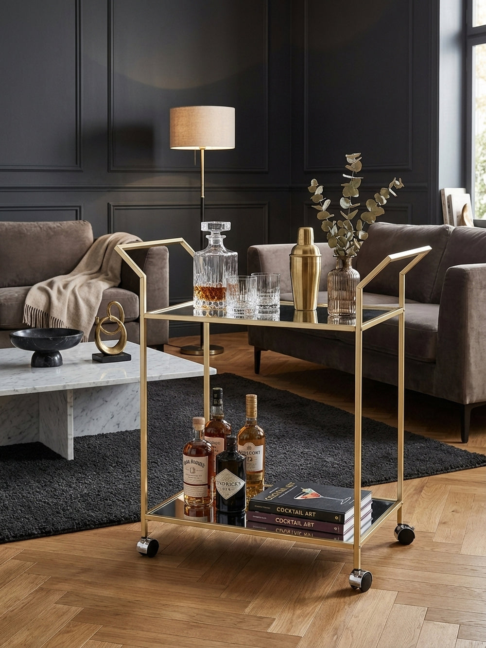 Eleganter Design Servierwagen in Gold, stilvoll arrangiert mit Gläsern und Dekantern in einem modernen Wohnzimmer mit dunkler Wand._