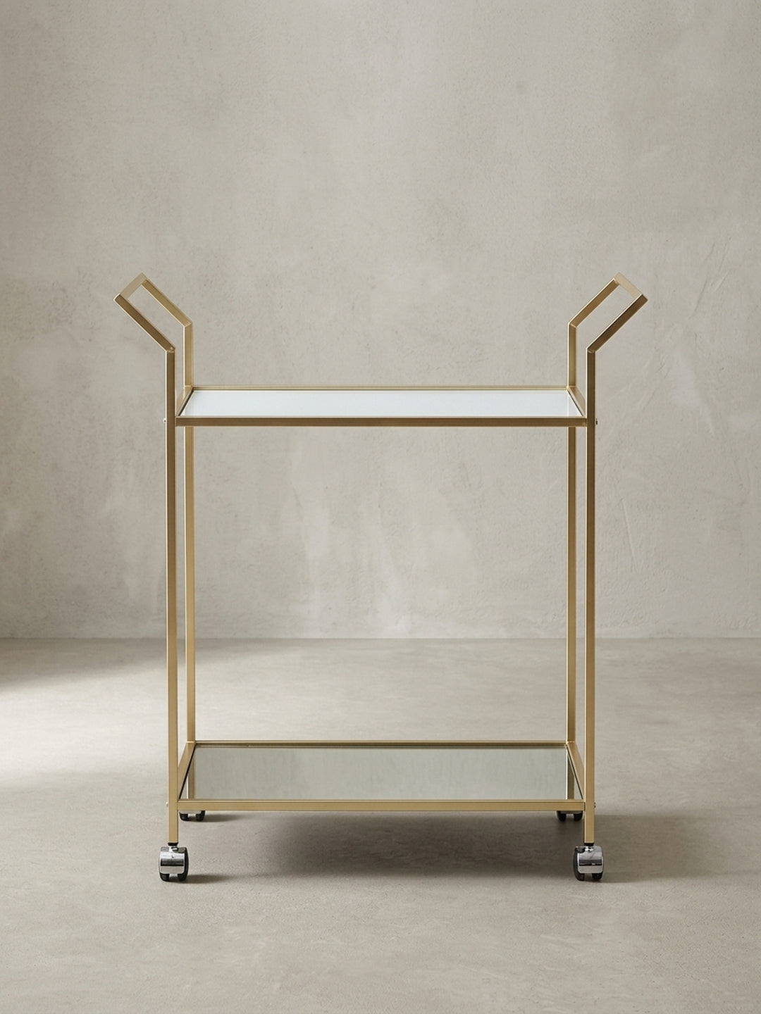 Goldener Servierwagen aus Metall und Glas vor weißem Hintergrund, der die klaren Linien und das glamouröse Design hervorhebt._