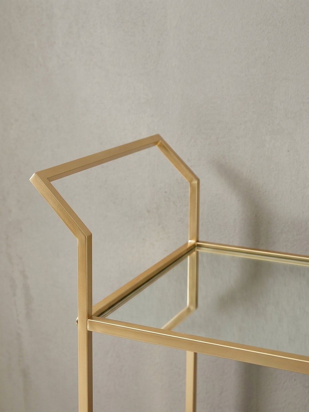 Detailaufnahme des eckigen Griffs des goldenen Servierwagens, der die präzise Verarbeitung des lackierten Metalls verdeutlicht._