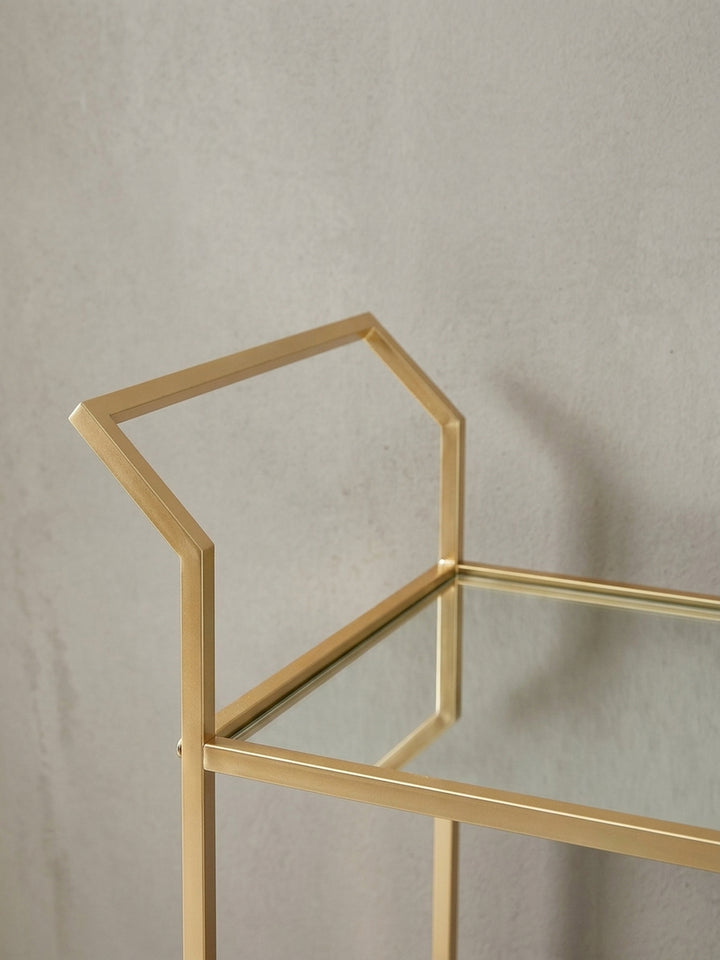 Detailaufnahme des eckigen Griffs des goldenen Servierwagens, der die präzise Verarbeitung des lackierten Metalls verdeutlicht._