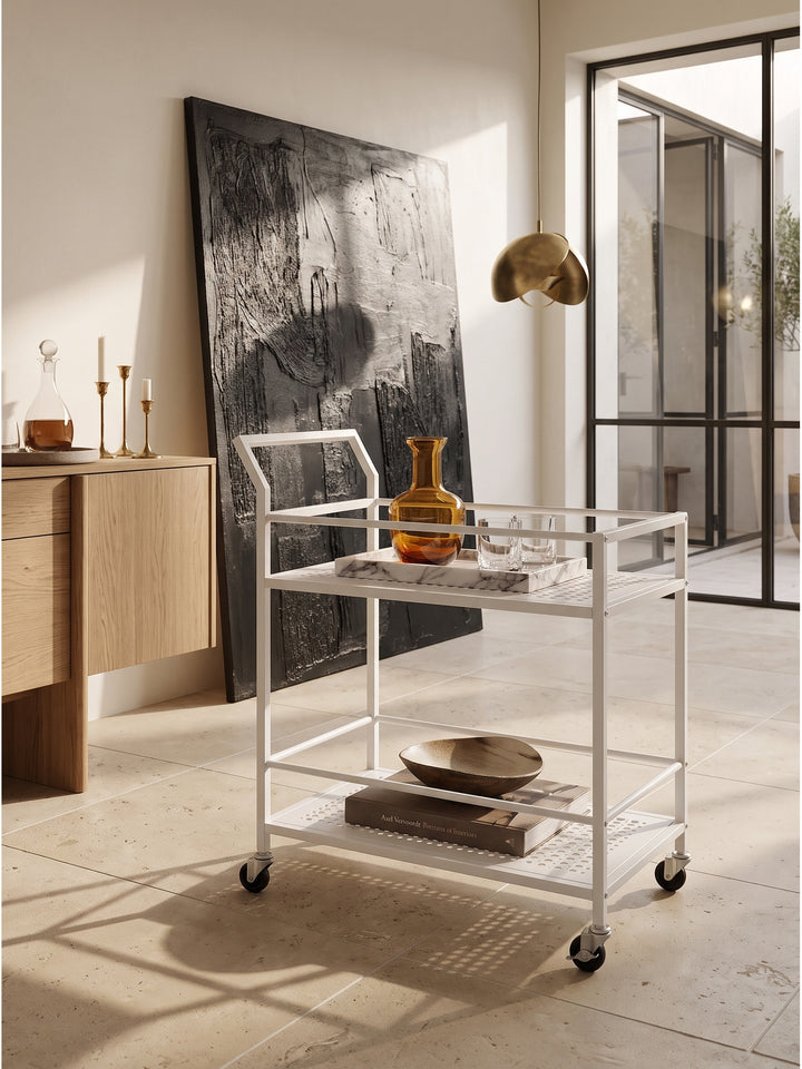 Stilvoller weißer Teewagen aus Metall angerichtet als elegante Hausbar mit schweren Kristallgläsern auf einem Marmortablett_