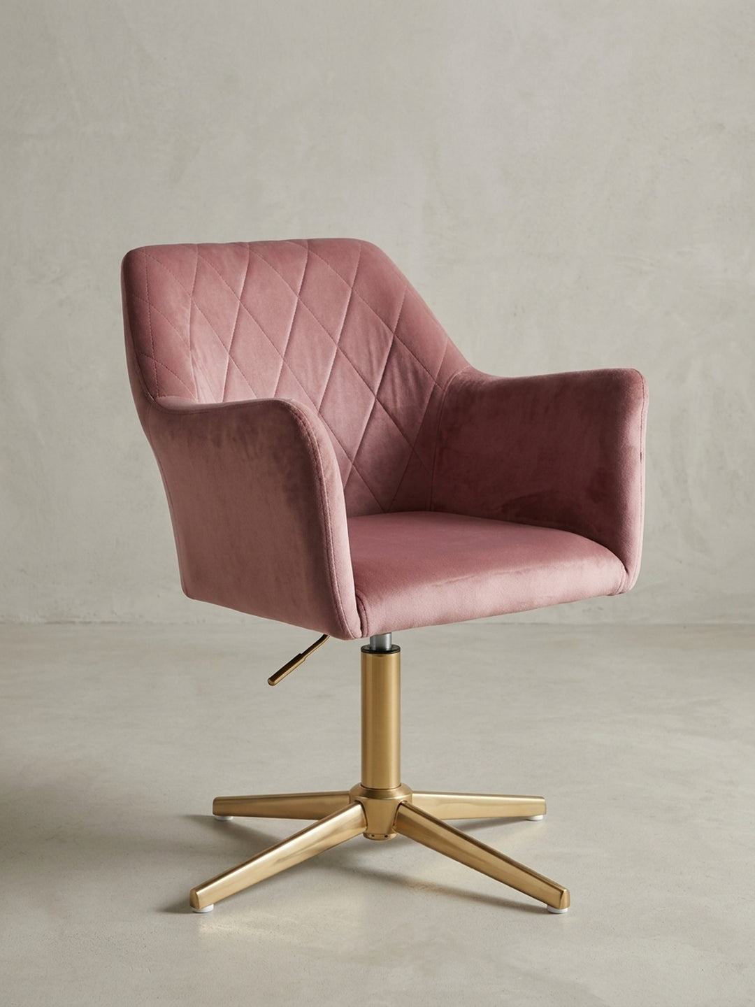 Der rosa Samt-Drehstuhl in einer 3/4-Ansicht, die die geschwungenen Armlehnen und die ergonomische Form der Rückenlehne zeigt, ideal für das Home-Office._