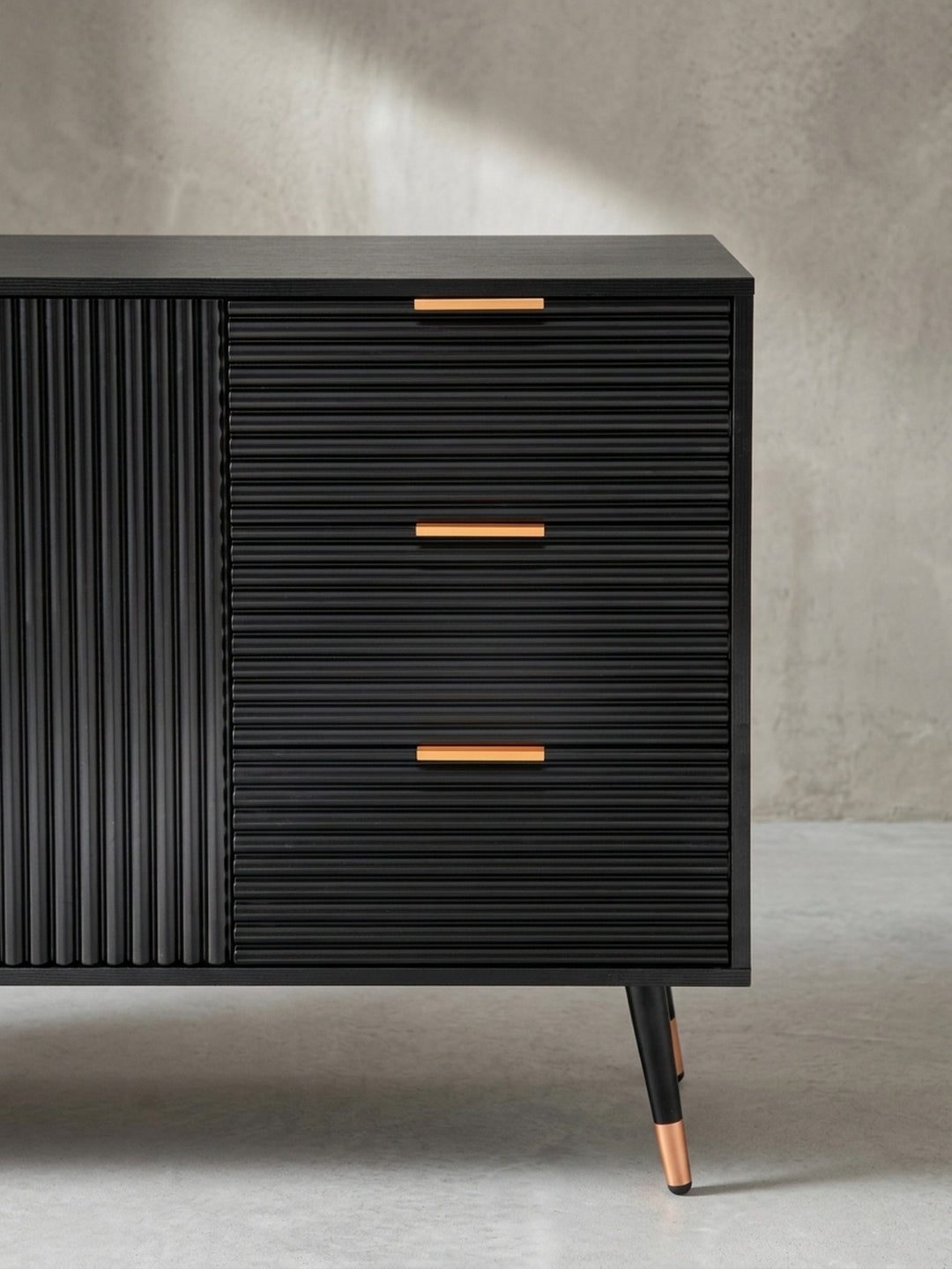 Nahaufnahme eines goldenen Schubladengriffs auf der geriffelten Front des schwarzen Sideboards, ein Detail, das modernen Luxus ausstrahlt._