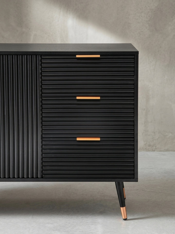 Nahaufnahme eines goldenen Schubladengriffs auf der geriffelten Front des schwarzen Sideboards, ein Detail, das modernen Luxus ausstrahlt._