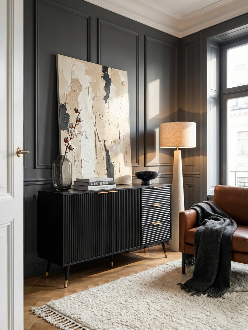 Schwarzes Sideboard mit Rillenfront und Goldgriffen als Blickfang in einem modern-klassischen Wohnzimmer mit Fischgrätparkett und Stuckdecke._