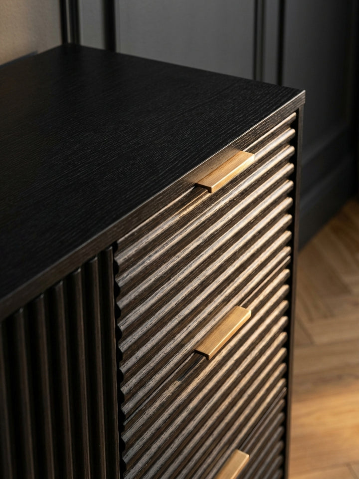 Detailaufnahme der markanten Holzmaserung des Sideboards in schwarzer Eiche-Optik, die durch das warme Licht einer Tischlampe betont wird._