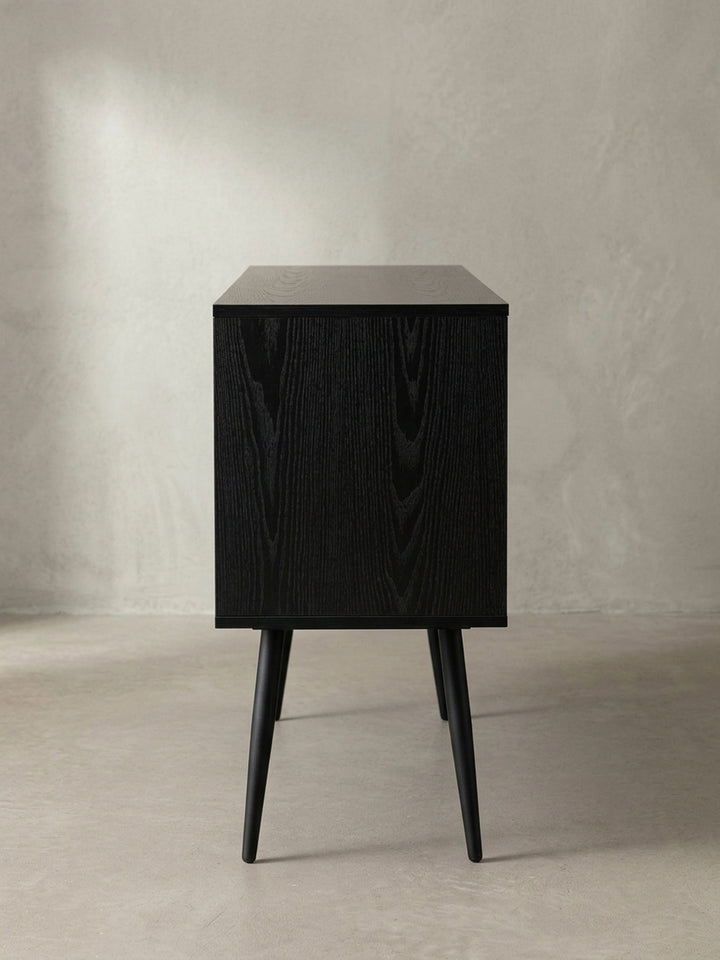 Nahaufnahme der runden, goldfarbenen Griffe aus lackiertem Eisen auf den Türen des schwarzen Sideboards, die einen warmen, metallischen Akzent auf dem dunklen Holzdekor setzen._