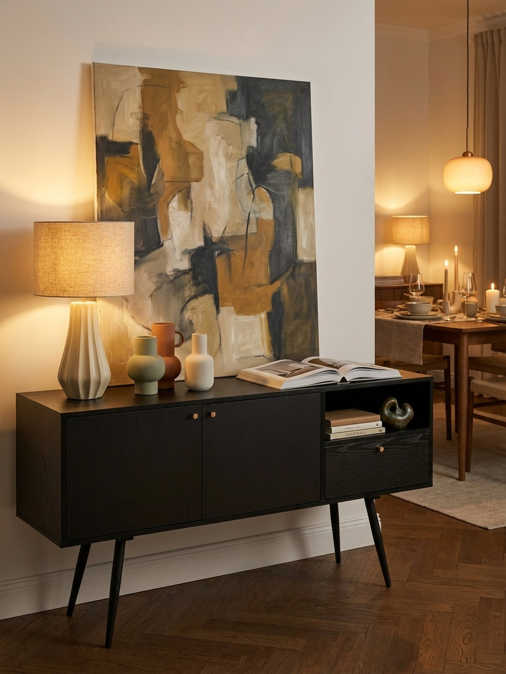 Eine moderne Tischlampe mit Keramikfuß und ein Stapel Kunstbücher schmücken die Oberfläche der schwarzen Kommode und schaffen eine stilvolle, wohnliche Atmosphäre._