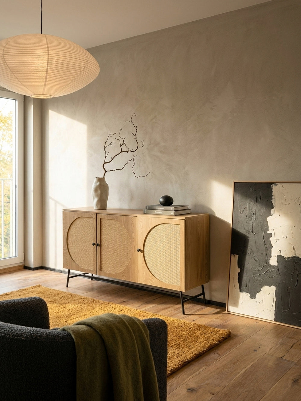 Modernes Sideboard in Eiche-Dekor mit Rattan-Geflecht in einem hellen, Japandi-inspirierten Wohnzimmer mit Holzboden und einer großen Reispapierleuchte._