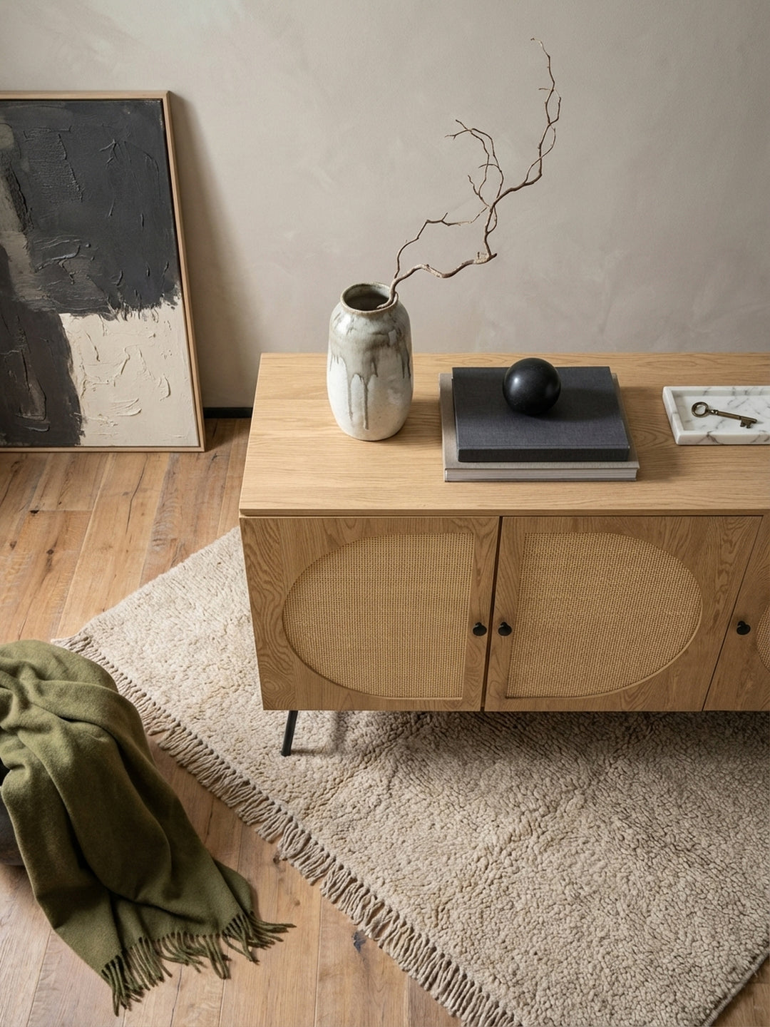 Draufsicht auf ein Wohnzimmer mit der Kommode aus Eichenholz und Rattan, die als Mittelpunkt neben einem grauen Sofa auf einem beigen Wollteppich steht._