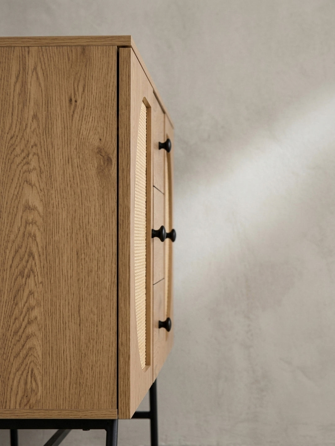 Nahaufnahme eines der runden, schwarzen Griffe an einer Schublade des Sideboards, der einen modernen Akzent auf dem Eichen-Dekor setzt._