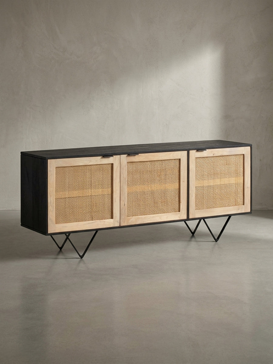 Schrägansicht des 175 cm breiten Sideboards aus schwarzem Mangoholz mit drei hellen Türen aus naturfarbenem Schilfrohrgeflecht._