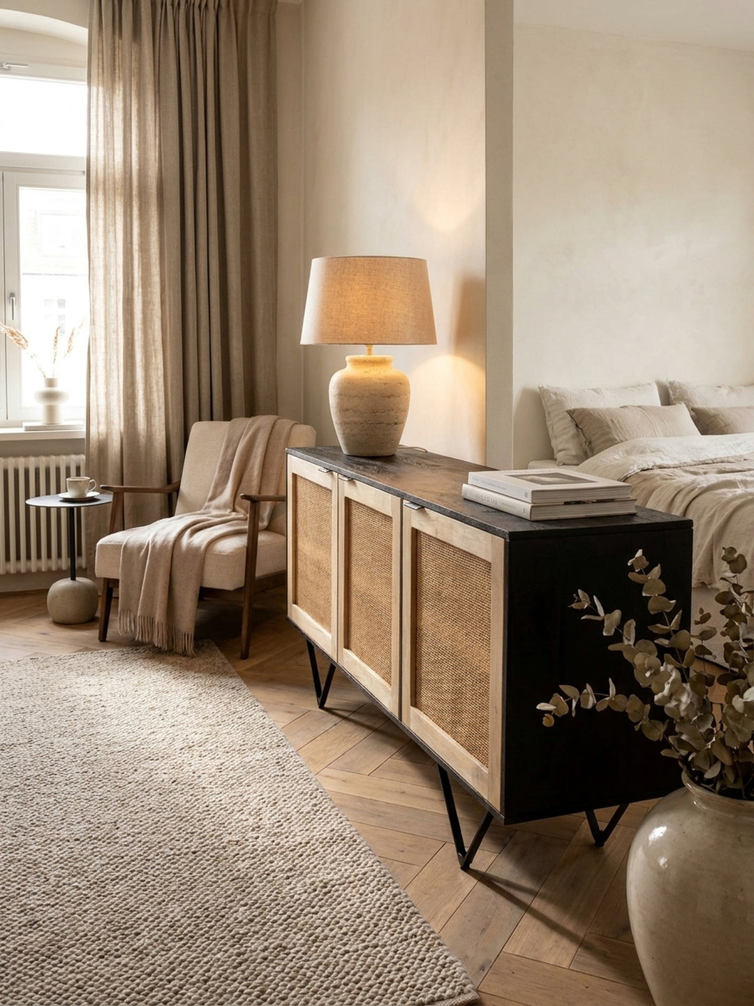Kombination aus Rattan-Kommode und einem beigen Leinen-Sessel im lichtdurchfluteten Raum mit architektonischen Stuckdetails._