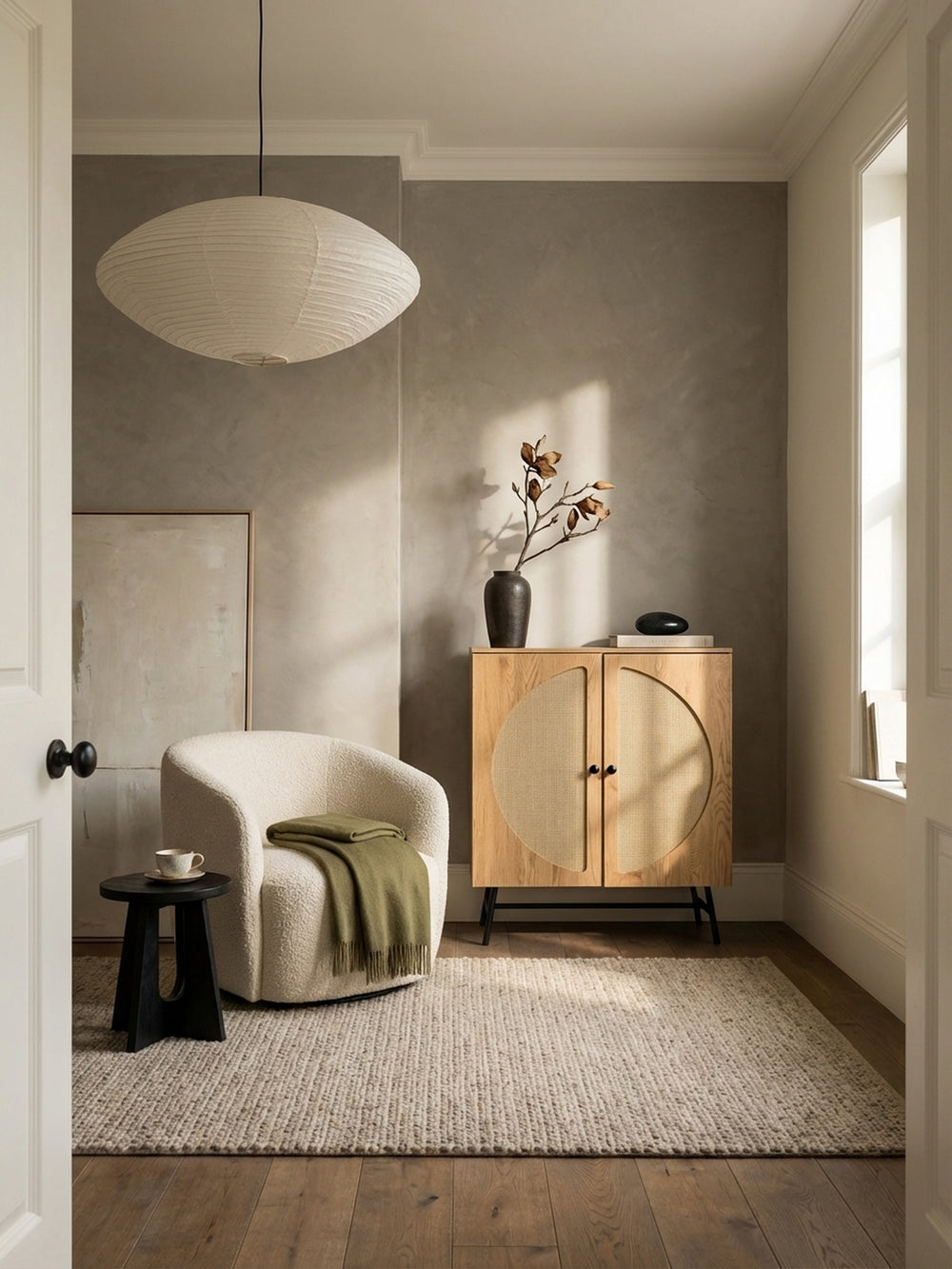 Hohes Sideboard im Japandi-Stil mit Rattan-Geflecht vor einer olivgrünen Wand in einem minimalistisch eingerichteten Wohnzimmer._