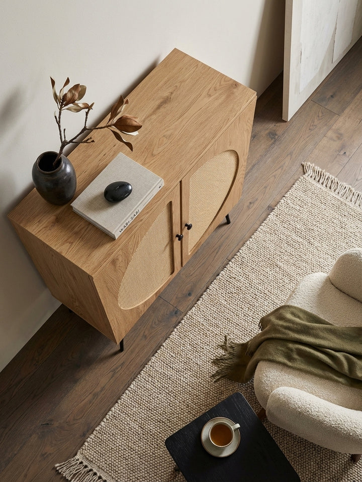 Blick von oben auf den Kommodenschrank mit Eiche-Dekor, platziert auf einem beigen Wollteppich neben einem cremefarbenen Sessel._
