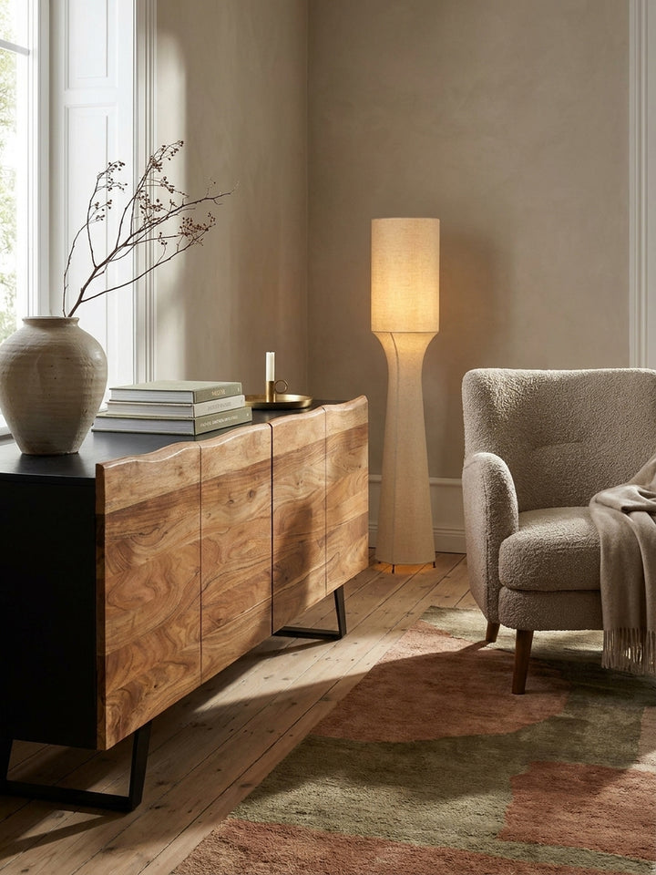 Das 180 cm breite Sideboard aus Akazie und Metall als harmonische Ergänzung zu einem minimalistischen schwarzen Bodenleuchter mit Leinenschirm._