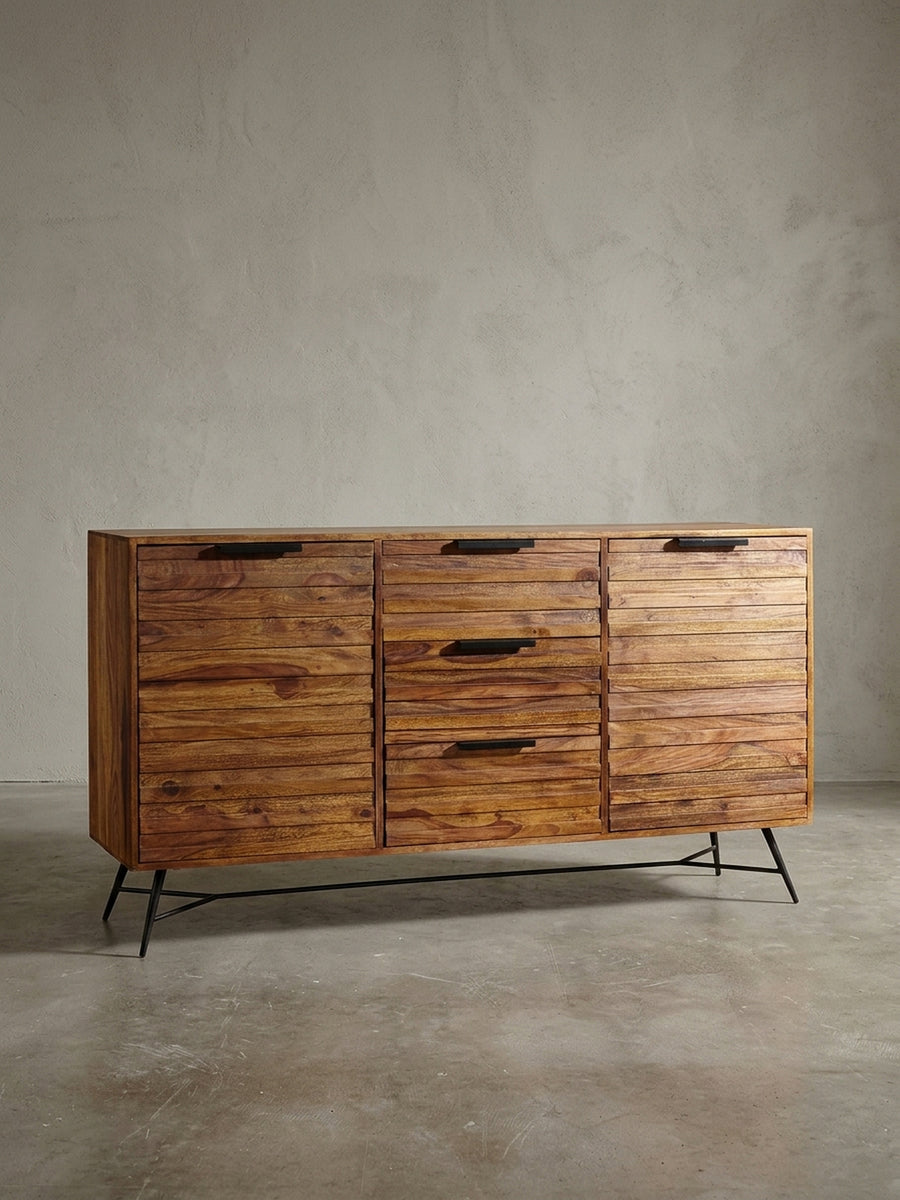 Breites Massivholz Sideboard im Industrial Design freigestellt. Drei Schubladen und zwei Türen mit Rillenfront ruhen auf einem filigranen, schwarz lackierten Metallgestell mit Querstrebe._