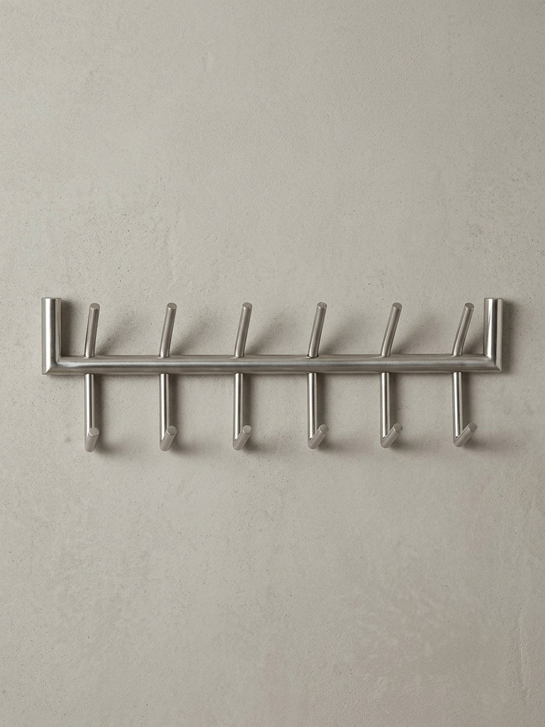Die Design Hakenleiste in einer 3/4-Ansicht, die die räumliche Tiefe von 10 cm und die versetzte Anordnung der oberen und unteren Garderobenhaken aus Metall darstellt._