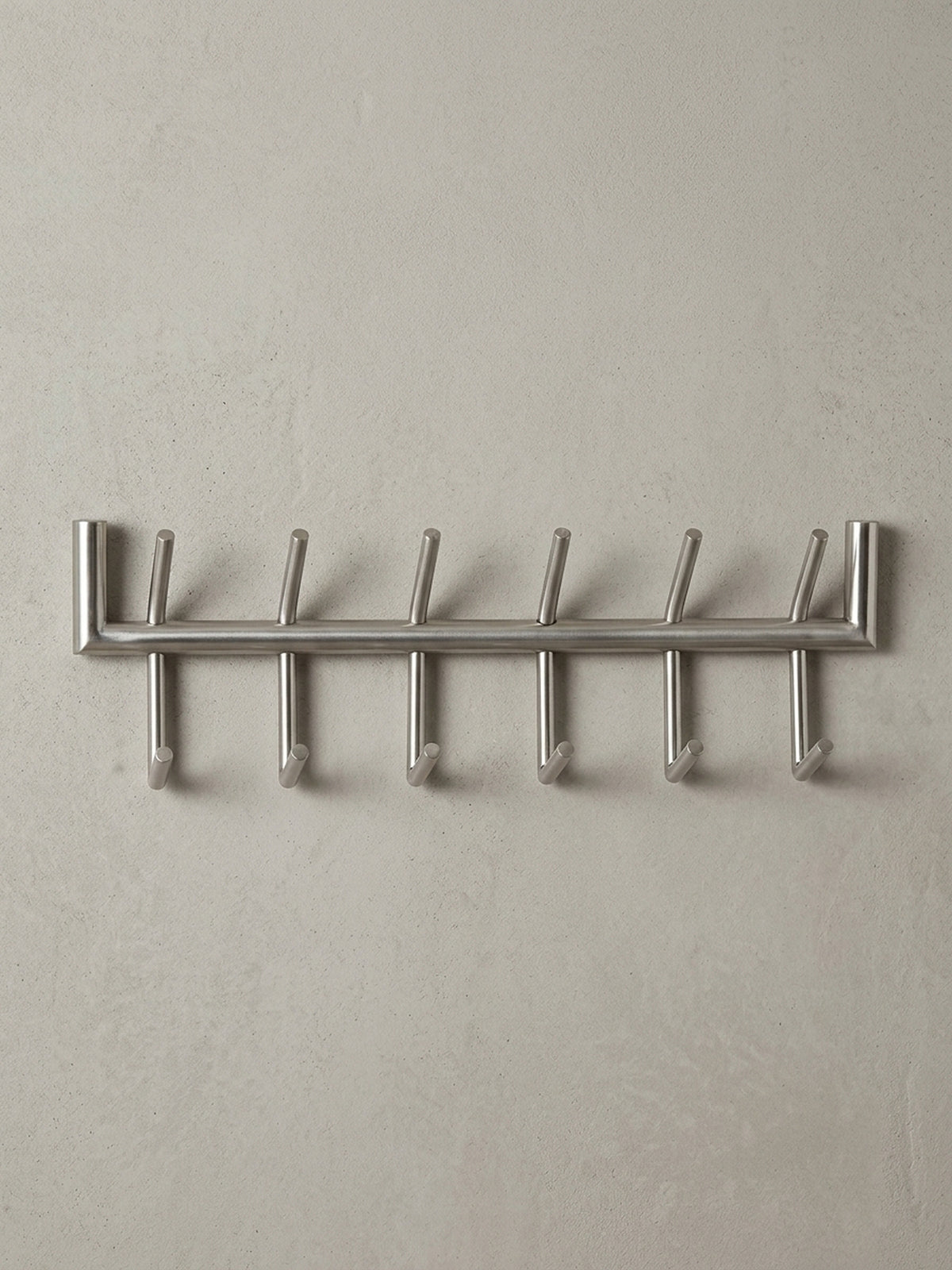 Die Design Hakenleiste in einer 3/4-Ansicht, die die räumliche Tiefe von 10 cm und die versetzte Anordnung der oberen und unteren Garderobenhaken aus Metall darstellt._