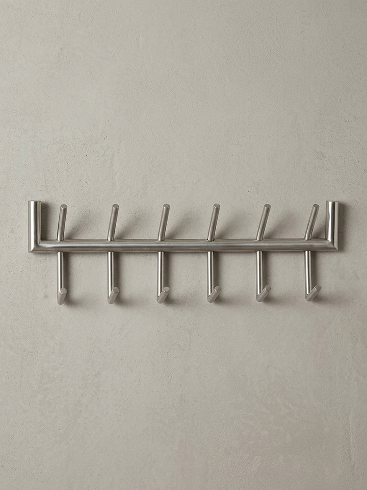 Die Design Hakenleiste in einer 3/4-Ansicht, die die räumliche Tiefe von 10 cm und die versetzte Anordnung der oberen und unteren Garderobenhaken aus Metall darstellt._