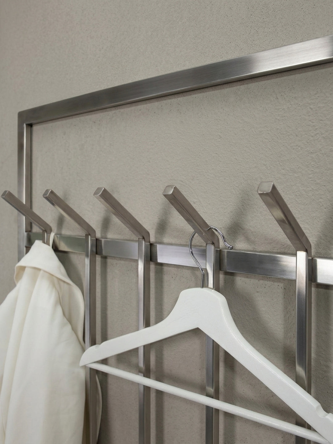 Eine alternative Perspektive der Wandgarderobe aus Metall, die das Spiel von Licht und Schatten auf der matt polierten Oberfläche betont._