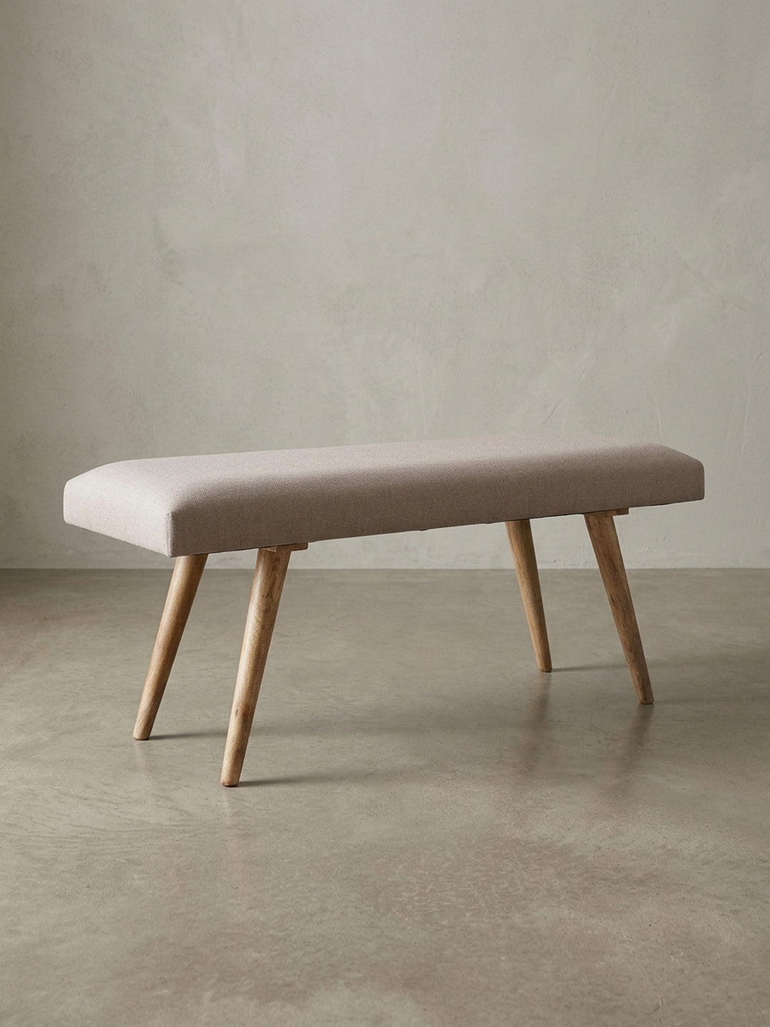 Beige Stoffbank im Retro-Stil frontal freigestellt. Die klare rechteckige Form, das 12 cm dicke Polster und die konischen Massivholzbeine unterstreichen das zeitlose Design._