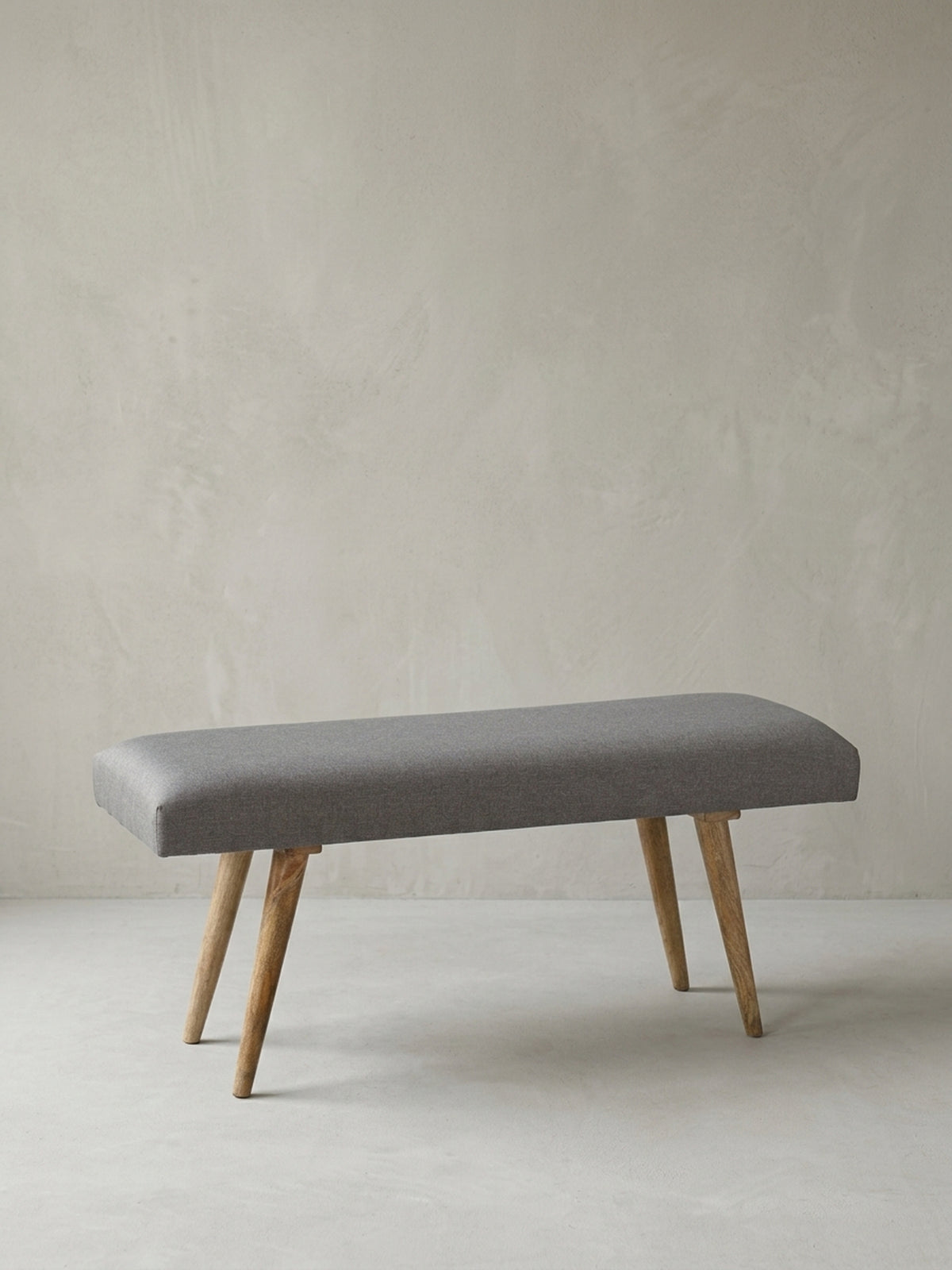 Alternative Perspektive der gepolsterten Zweisitzer-Bank aus Stoff und Holz. Die ausgewogenen Proportionen des 117x51x38 cm großen Möbelstücks vereinen Funktionalität mit dezenter Eleganz._
