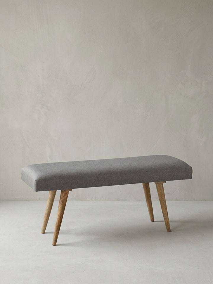 Alternative Perspektive der gepolsterten Zweisitzer-Bank aus Stoff und Holz. Die ausgewogenen Proportionen des 117x51x38 cm großen Möbelstücks vereinen Funktionalität mit dezenter Eleganz._