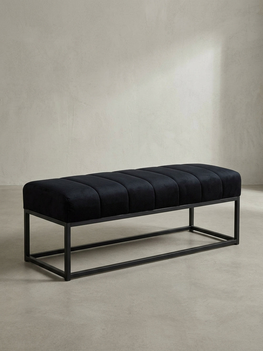 Moderne Sitzbank mit schwarzem Samtbezug und geradlinigem Metallgestell, freigestellt vor weißem Hintergrund aus einer Dreiviertel-Ansicht._