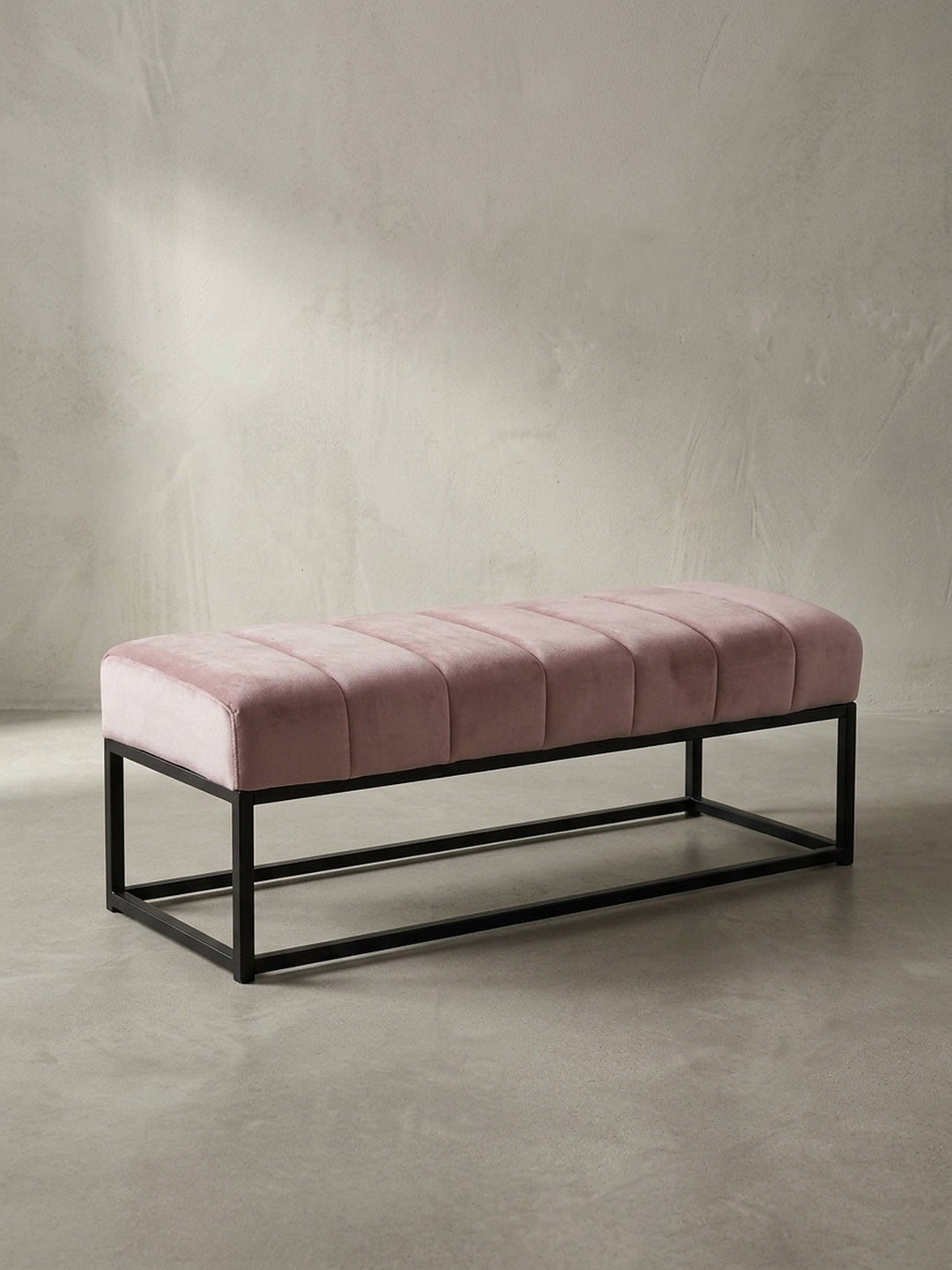 Frontansicht der Design-Sitzbank mit rosa Samtpolster und minimalistischem schwarzem Metallgestell, freigestellt vor weißem Hintergrund._