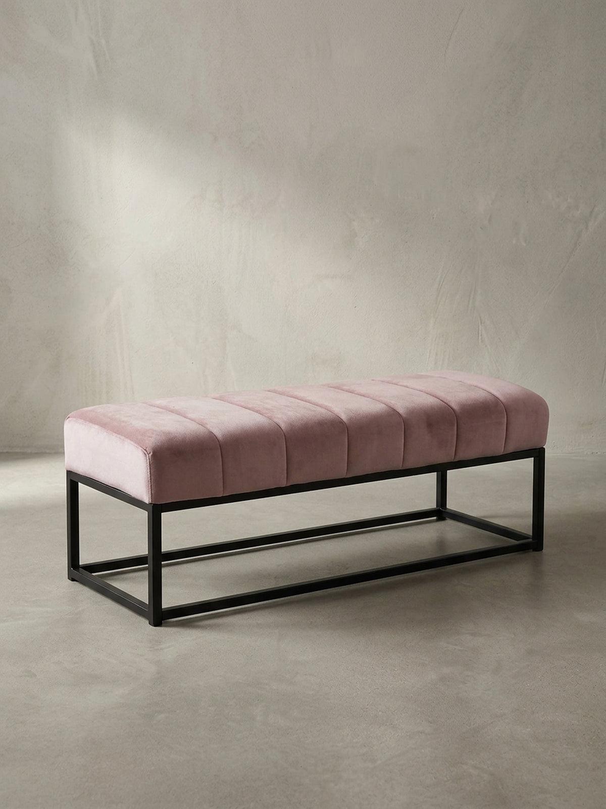 Frontansicht der Design-Sitzbank mit rosa Samtpolster und minimalistischem schwarzem Metallgestell, freigestellt vor weißem Hintergrund._