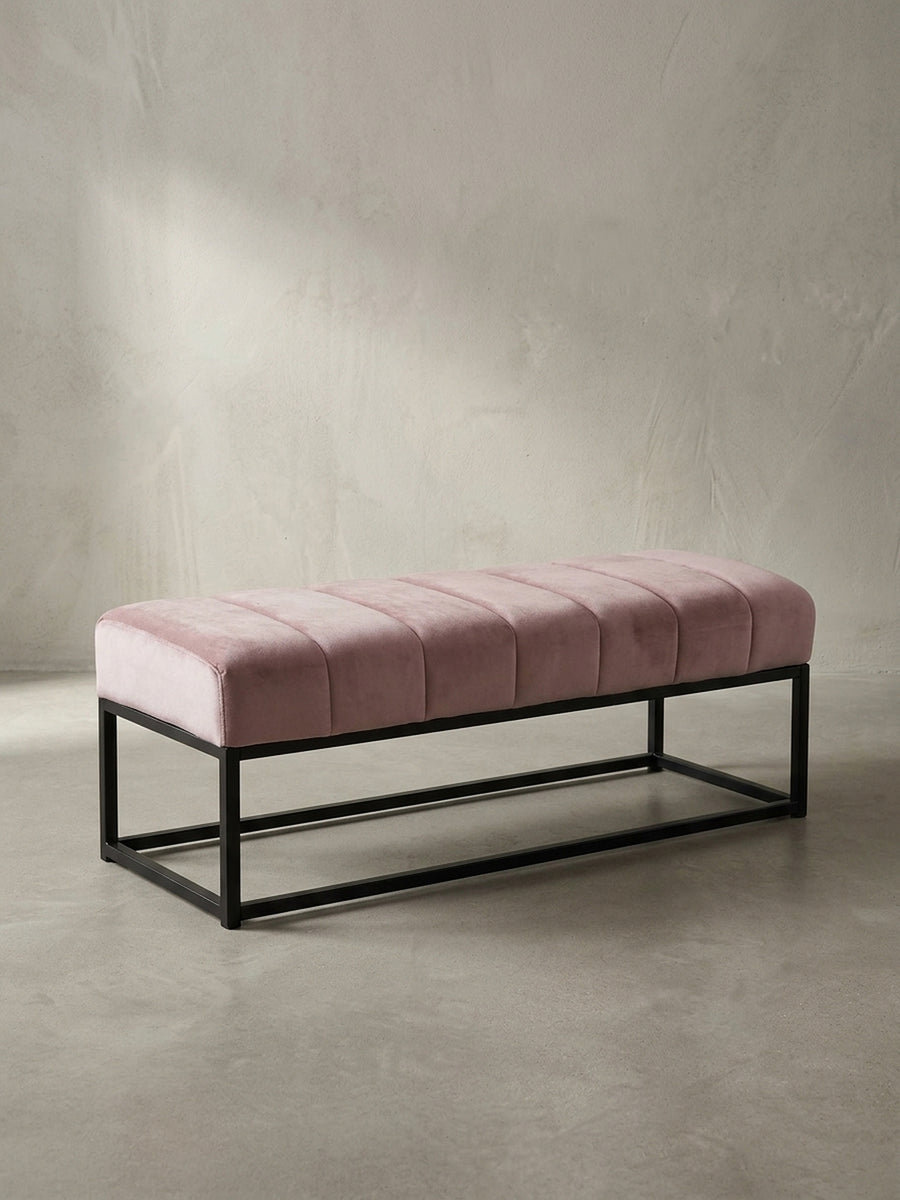 Frontansicht der Design-Sitzbank mit rosa Samtpolster und minimalistischem schwarzem Metallgestell, freigestellt vor weißem Hintergrund._