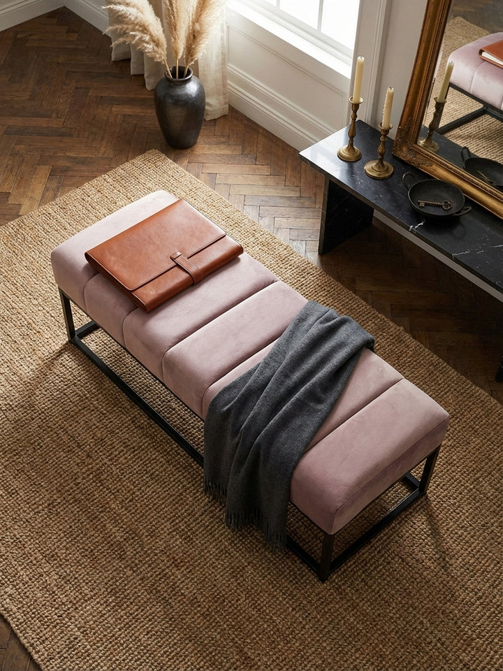 Draufsicht auf die gesteppte Polsterbank aus rosa Samt auf einem Juteteppich, elegant arrangiert vor einer Wand mit Boiserie-Verkleidung._