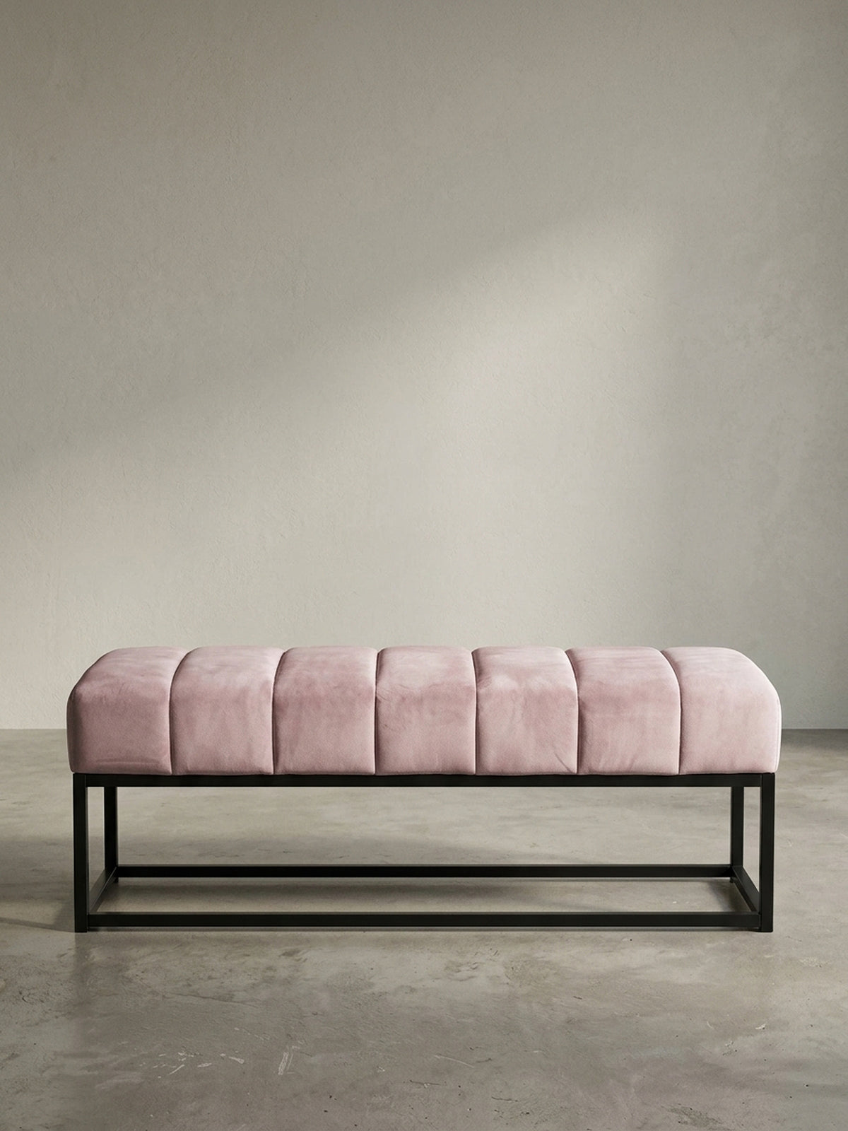 Schräge 3/4-Ansicht der rosa Samt-Polsterbank, die die Tiefe der gesteppten Sitzfläche und die klare Linienführung des Gestells zeigt._