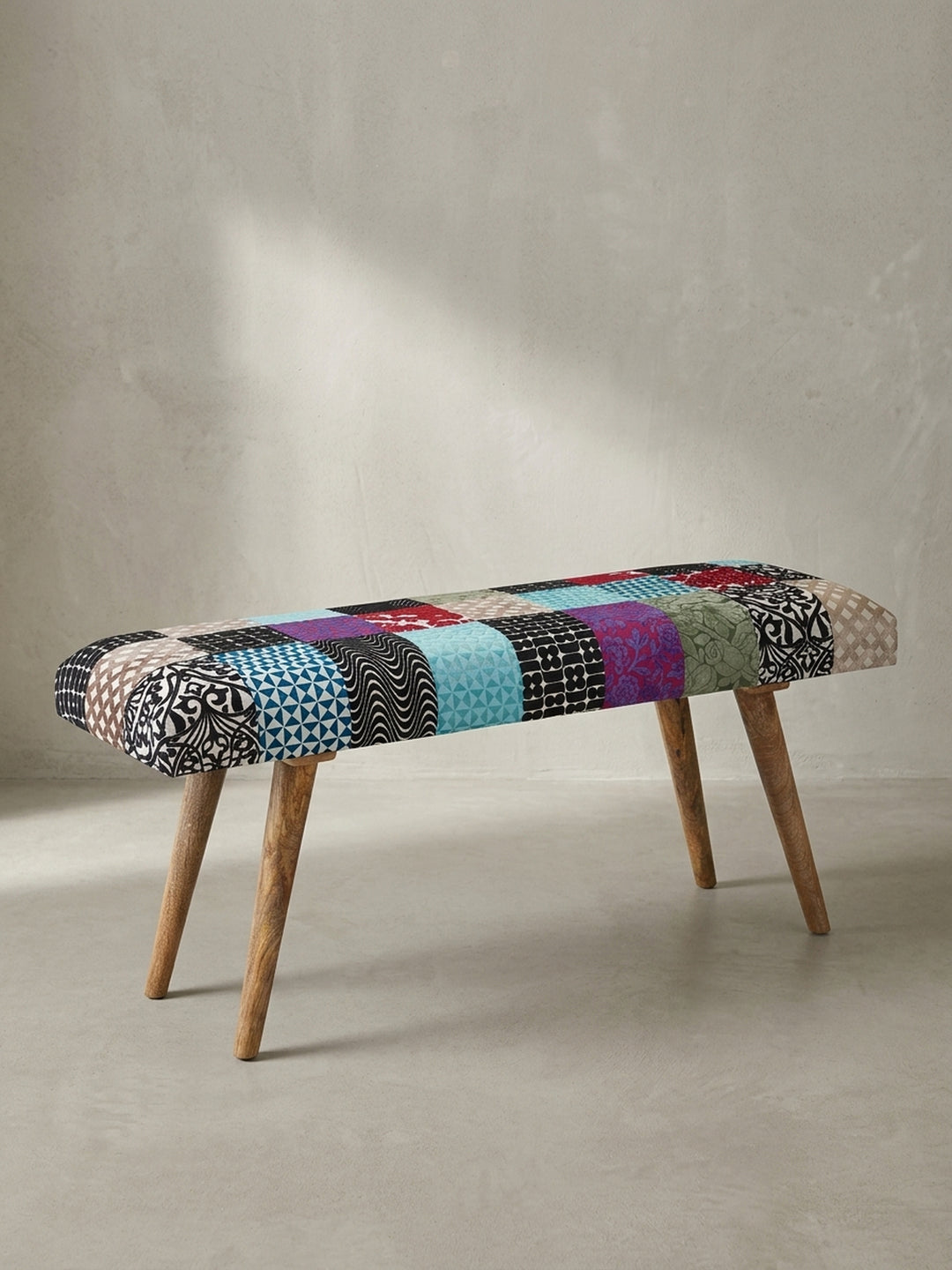 Bunte Patchwork-Sitzbank mit Füßen aus massivem Mangoholz 117x51x38 cm in der abgewinkelten Ansicht vor neutralem weißem Hintergrund._
