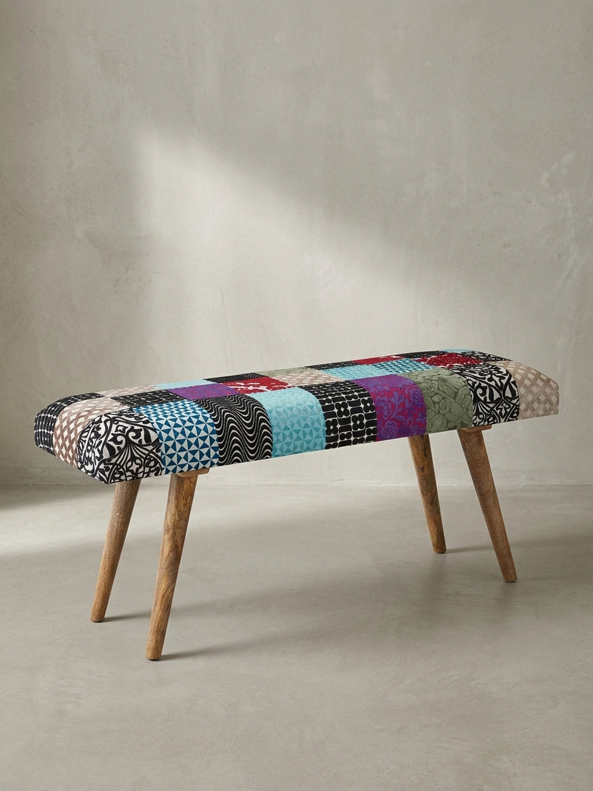 Bunte Patchwork-Sitzbank mit Füßen aus massivem Mangoholz 117x51x38 cm in der abgewinkelten Ansicht vor neutralem weißem Hintergrund.