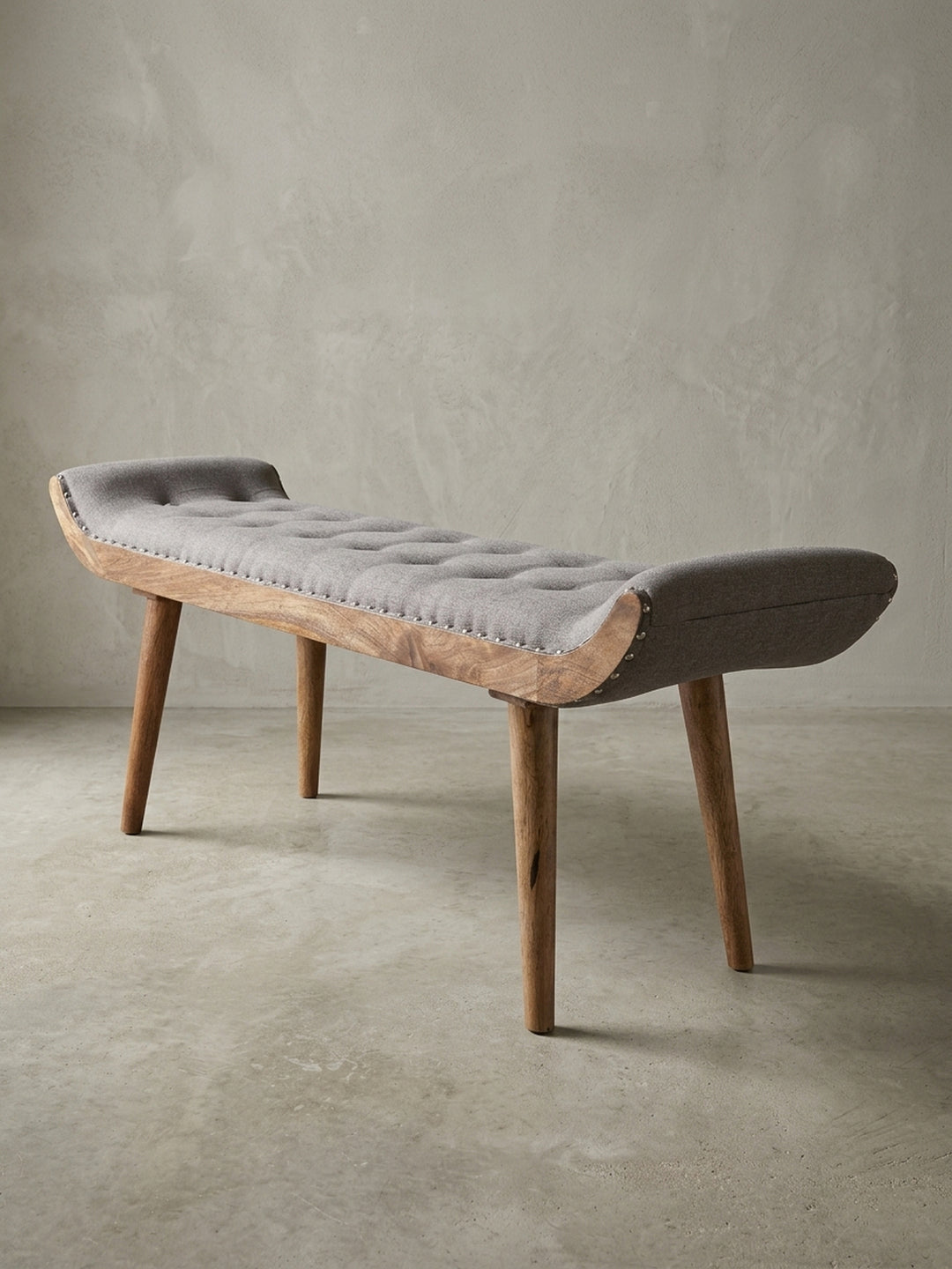 Studioaufnahme einer grauen Sitzbank 125x51x38 cm mit Chesterfield-Steppung und Holzbeinen, freigestellt vor weißem Hintergrund aus einer frontalen 3/4-Ansicht._