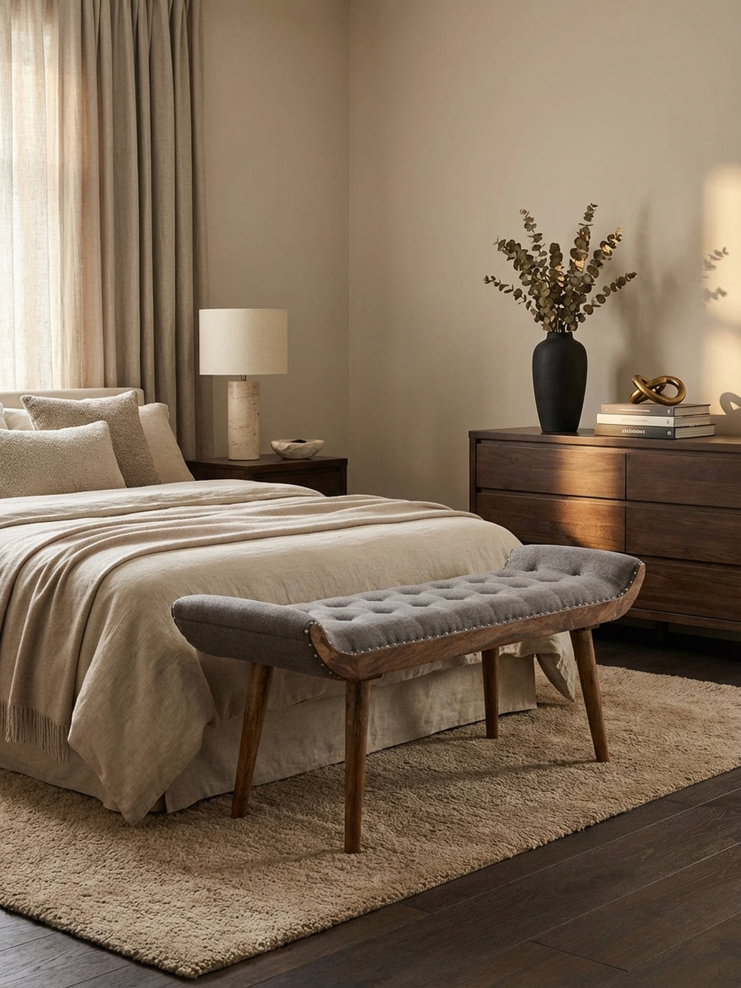 Elegante Sitzbank aus grauem Stoff im Chesterfield-Design, platziert am Fußende eines Bettes in einem luxuriös eingerichteten Schlafzimmer mit Holzboden und sanftem Licht._
