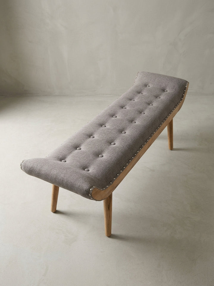 Alternative Perspektive auf die moderne Stoffbank, die die Symmetrie des Designs und die handwerkliche Qualität der Nietenverzierung entlang des Holzrahmens zur Geltung bringt._