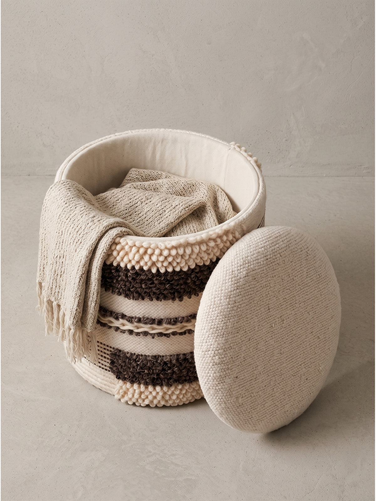 Texturierter Stauraumhocker mit Wollbezug in Beige und Dunkelbraun leicht schräg von der Seite im Fotostudio aufgenommen.