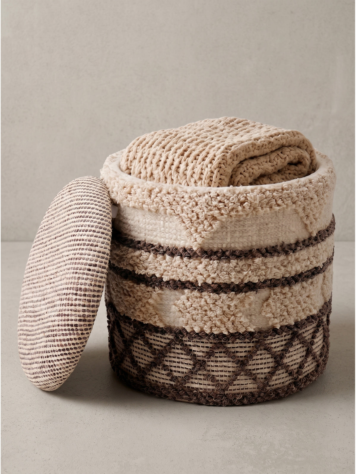 Runder Boho-Sitzhocker 40x40x45 cm aus beiger Wolle mit braunen Ornamenten und halb abgenommenem Deckel auf weißem Hintergrund.