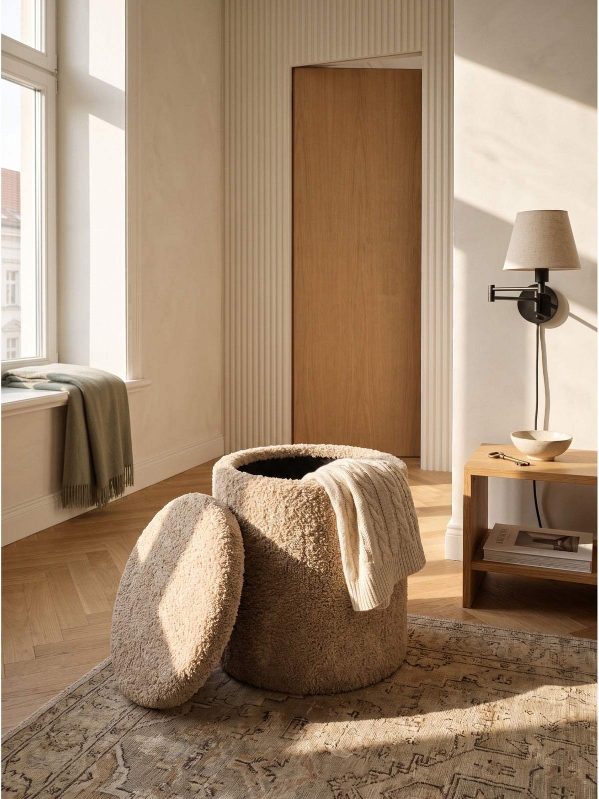 Großzügiges Schlafzimmer im Organic-Modern-Stil mit einem beigen Sitzhocker aus zotteligem Wollstoff neben einem gemütlichen Lesesessel._
