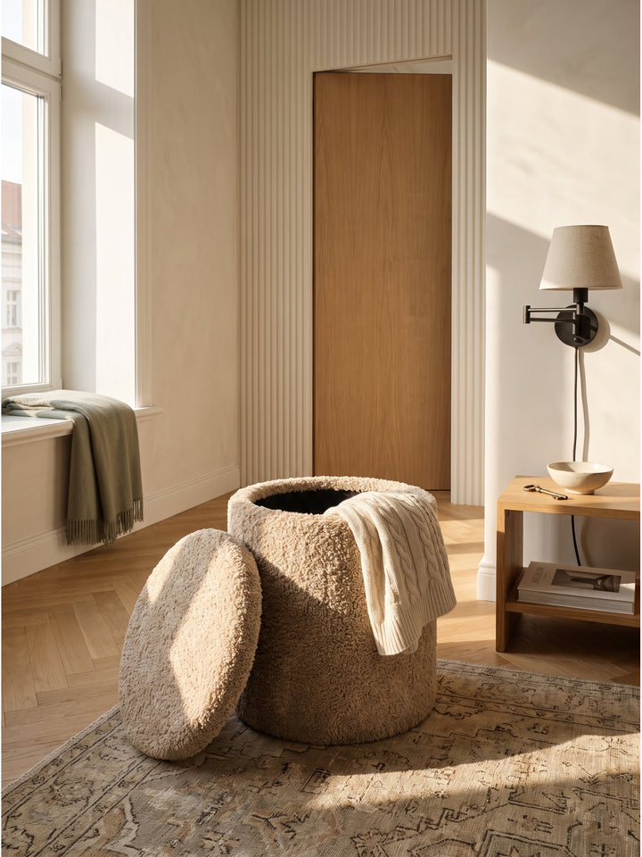 Großzügiges Schlafzimmer im Organic-Modern-Stil mit einem beigen Sitzhocker aus zotteligem Wollstoff neben einem gemütlichen Lesesessel._